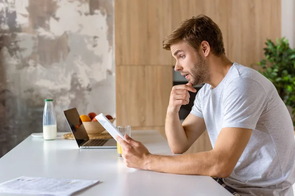 Seitenansicht eines jungen Mannes, der am Küchentisch mit einem digitalen Tablet spricht — Stockfoto