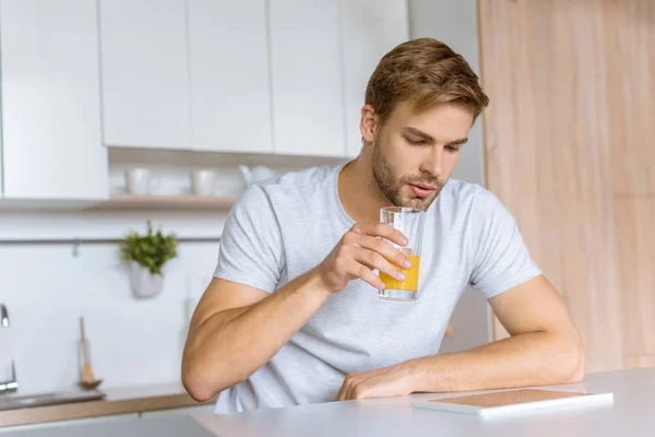 Hombre beber jugo fresco durante el desayuno en la mesa de la cocina con la tableta digital - foto de stock