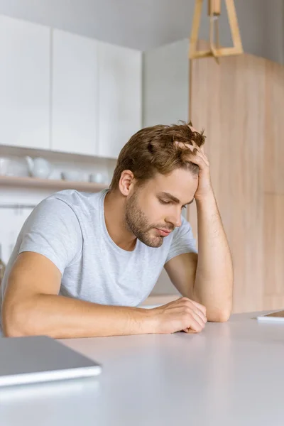 Chateado jovem sentado na mesa da cozinha com laptop — Fotografia de Stock