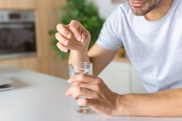 Abgeschnittenes Bild eines Mannes, der am Küchentisch Tabletten mit Wasser ins Glas gibt — Stockfoto