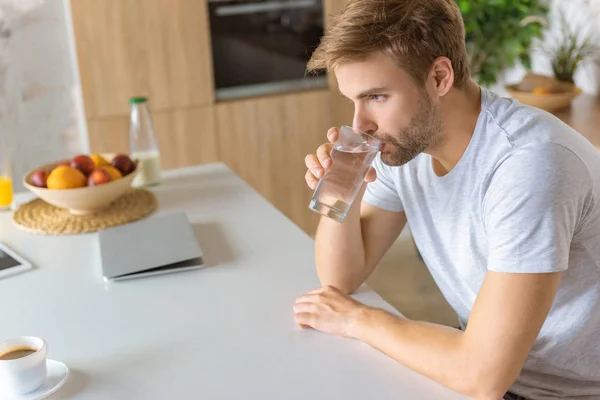 Enfoque selectivo del joven beber agua en la mesa de la cocina - foto de stock
