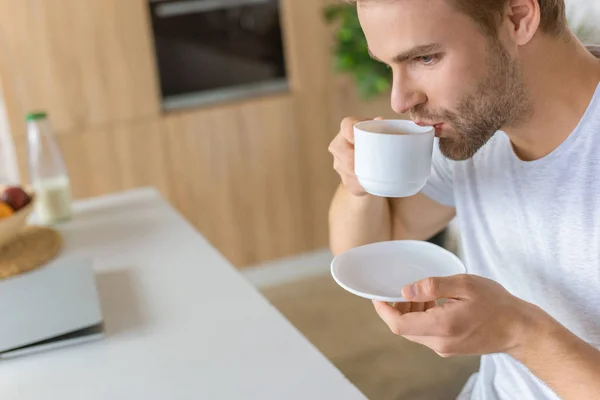 Foco seletivo do jovem bebendo café na cozinha — Fotografia de Stock