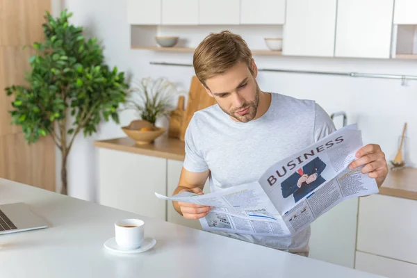 Hombre leyendo el periódico durante la mañana en la mesa de la cocina con taza de café - foto de stock