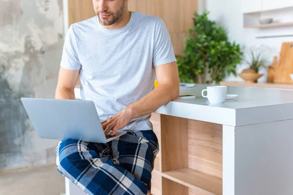 Imagen recortada del hombre usando el ordenador portátil en la cocina - foto de stock