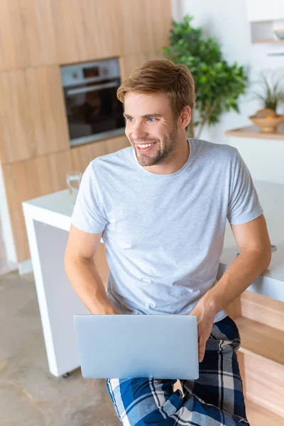 Homem bonito feliz usando laptop na cozinha — Fotografia de Stock
