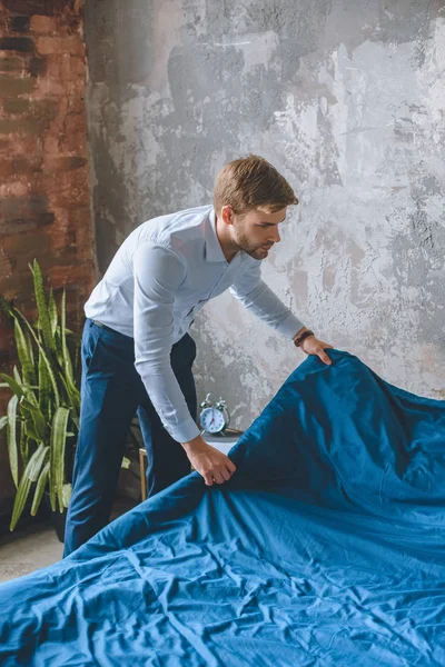 Молодий бізнесмен покриває ліжко синім покриттям вдома — стокове фото