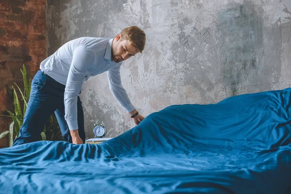 Молодой бизнесмен, делающий кровать в спальне дома — стоковое фото