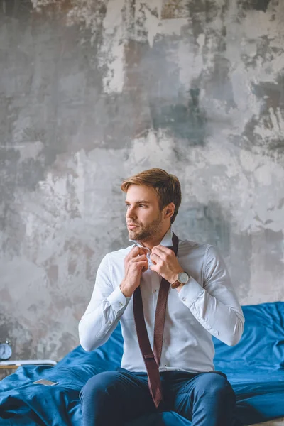 Serious businessman tying necktie in bedroom at home — Stock Photo