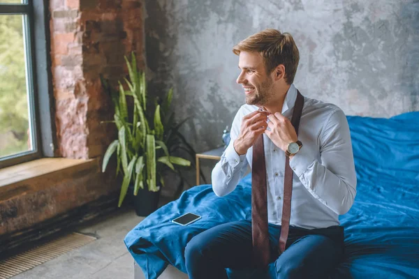 Smiling businessman tying necktie in bedroom at home — Stock Photo