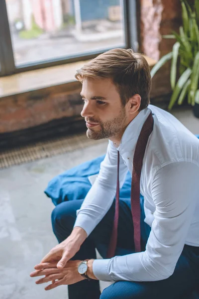 Selektiver Fokus eines lächelnden Geschäftsmannes, der mit Krawatte über dem Hals im heimischen Schlafzimmer sitzt — Stockfoto