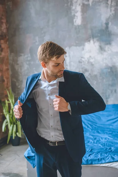 Serious businessman putting on jacket in bedroom at home — Stock Photo