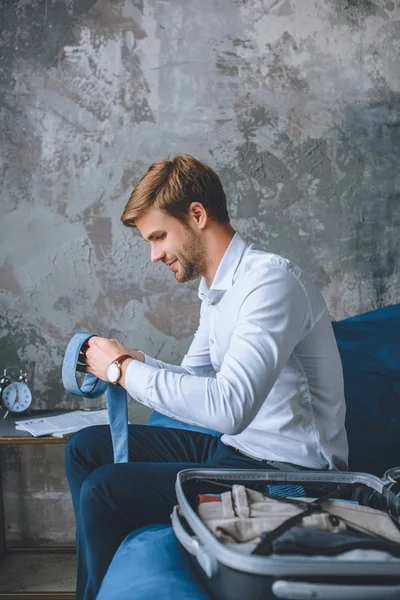 Lächelnder Geschäftsmann, der zu Hause im Schlafzimmer Gepäck in Koffer packt — Stockfoto