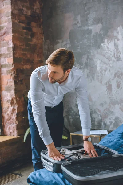 Business man looking away and packing luggage in suitcase in bedroom at home — стоковое фото