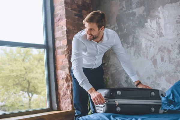 Усміхнений молодий бізнесмен закриває валізу в спальні вдома — Stock Photo