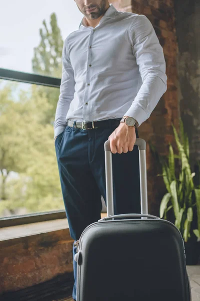 Imagen recortada de turista masculino de pie con maleta en casa - foto de stock