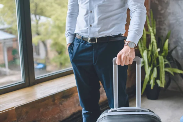 Abgeschnittenes Bild eines Geschäftsmannes mit Hand in Tasche, der mit Koffer zu Hause steht — Stockfoto