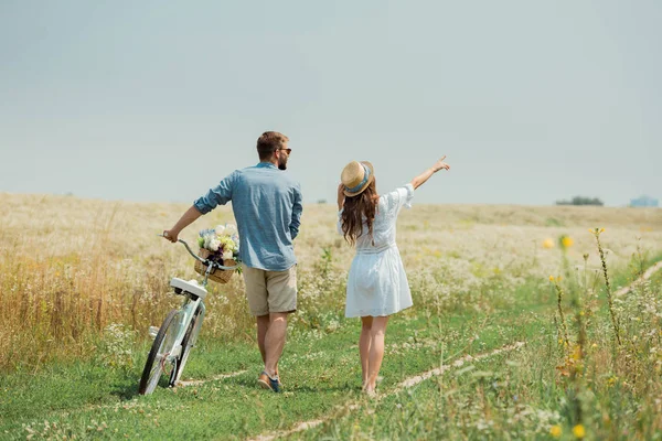 Vue arrière du couple avec vélo rétro dans le champ d'été avec des fleurs sauvages — Photo de stock