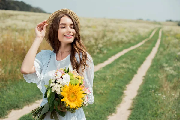 Portrait of smiling woman in white dress with bouquet of wild flowers in field — Stock Photo