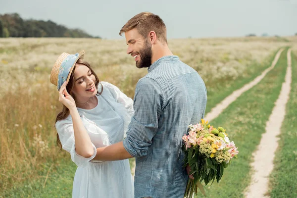 Sonriente hombre ocultar ramo de flores silvestres para novia detrás de vuelta en el campo de verano - foto de stock