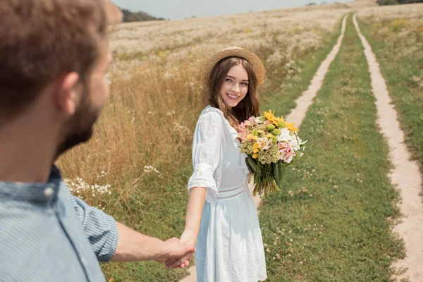 Teilansicht einer lächelnden Frau mit einem Strauß wilder Blumen und einem Freund, der Händchen hält im Feld — Stockfoto