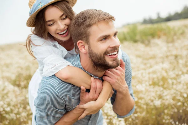 Happy lovers piggybacking together in filed with wild flowers — Stock Photo