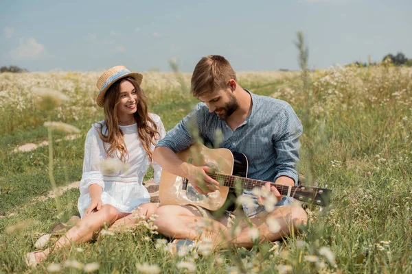 Man playing acoustic guitar to smiling girlfriend in summer filed — Stock Photo