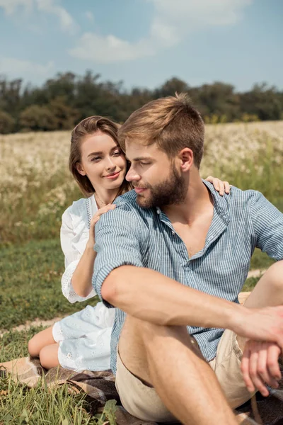 Jovem casal descansando no campo com flores selvagens no dia de verão — Fotografia de Stock