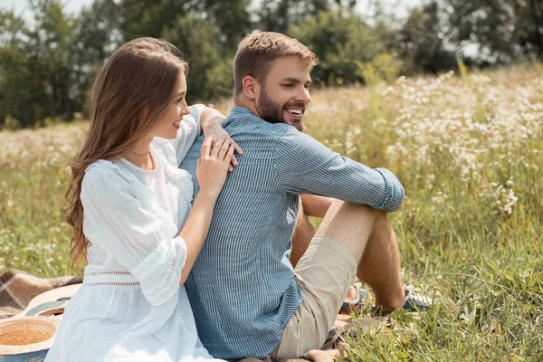 Couple souriant reposant dans le champ avec des fleurs sauvages le jour de l'été — Photo de stock