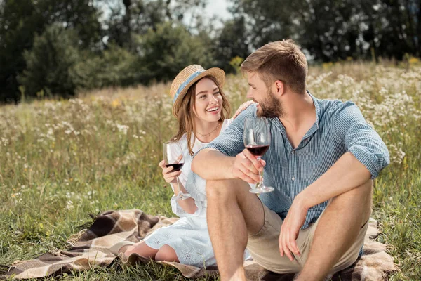 Sorrindo casal com copos de vinho tinto olhando um para o outro no campo de verão — Fotografia de Stock