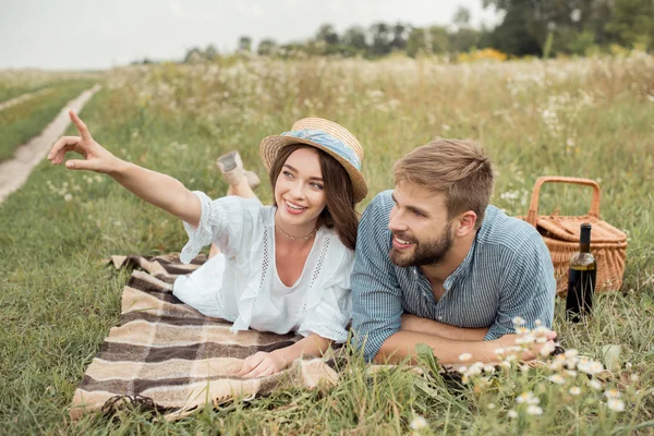 Sorrindo mulher mostrando algo para namorado enquanto descansa em cobertor juntos no campo de verão — Fotografia de Stock