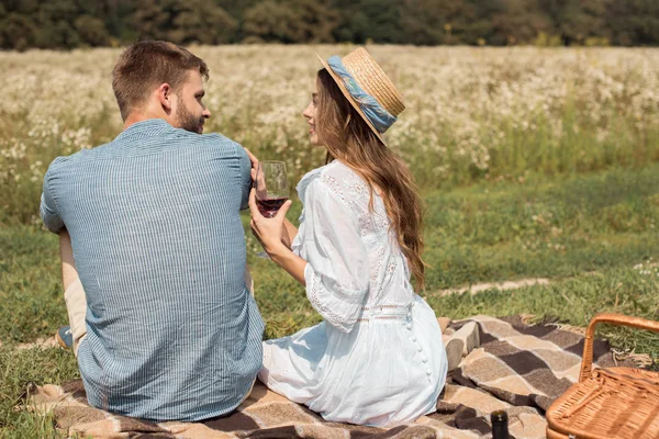 Atrás vista sonriente pareja teniendo picnic en el prado de verano con flores silvestres alrededor - foto de stock