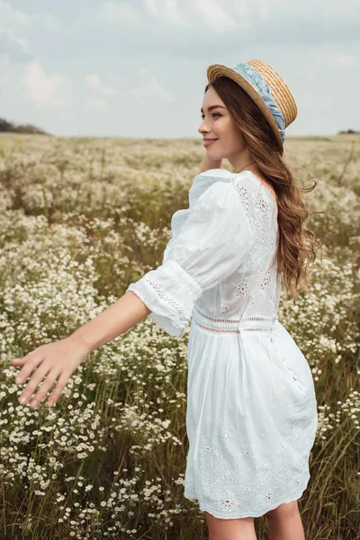 Bonita mujer en sombrero de paja y vestido blanco en el prado con flores silvestres - foto de stock