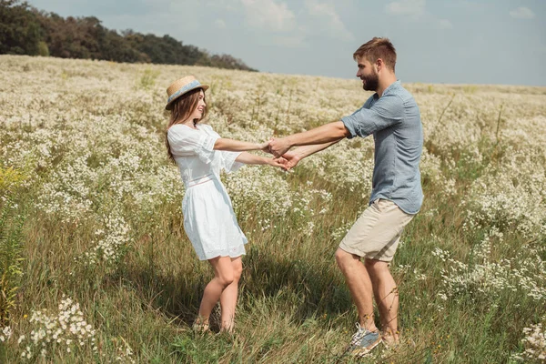 Seitenansicht des fröhlichen Paares Händchen haltend auf einer Wiese mit wilden Blumen — Stockfoto