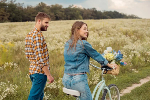 Vue latérale de jeunes amoureux avec vélo rétro dans le champ avec des fleurs sauvages — Photo de stock