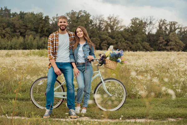 Jovens amantes com bicicleta retro no campo com flores silvestres — Fotografia de Stock