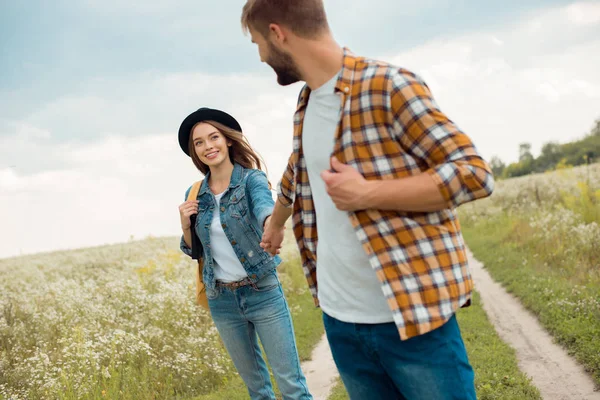 Amantes felices tomados de la mano en el campo con flores silvestres - foto de stock