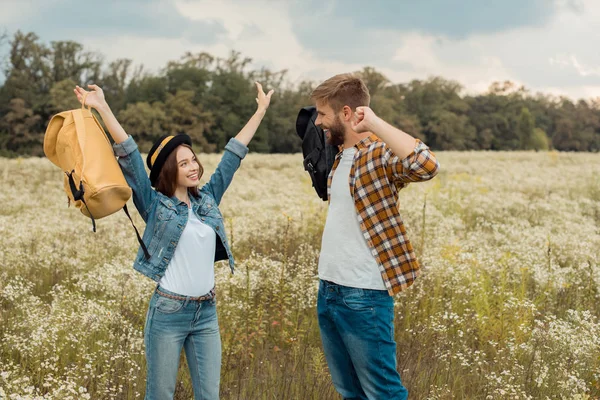 Cheerful couple with backpacks in summer field with wild flowers — Stock Photo