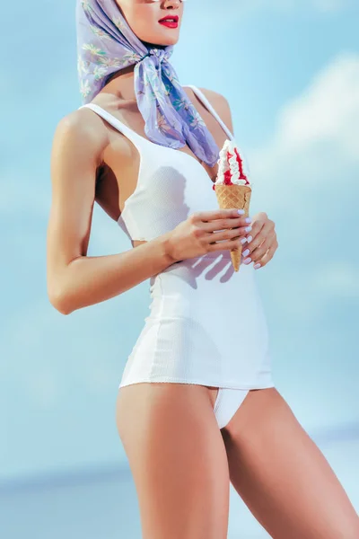 Vista cortada de menina atraente em roupa de banho retro e cachecol de seda segurando sorvete em cone de waffle — Fotografia de Stock