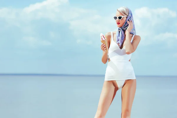 Belle fille mince en maillot de bain vintage tenant la crème glacée et posant près de la mer en été — Photo de stock