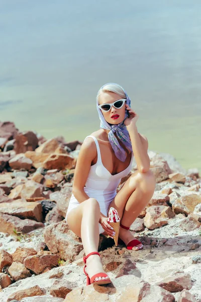 Hermosa joven en estilo retro posando en la playa rocosa con helado - foto de stock