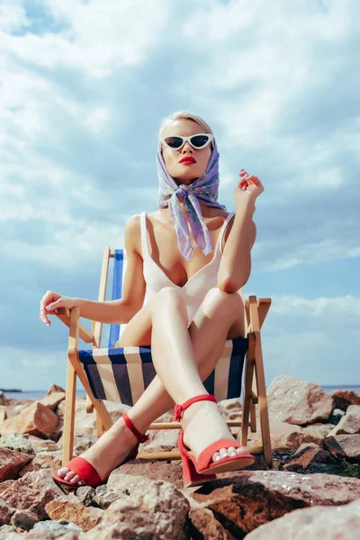 Vista inferior da menina atraente elegante em maiô retro sentado na cadeira de praia — Fotografia de Stock