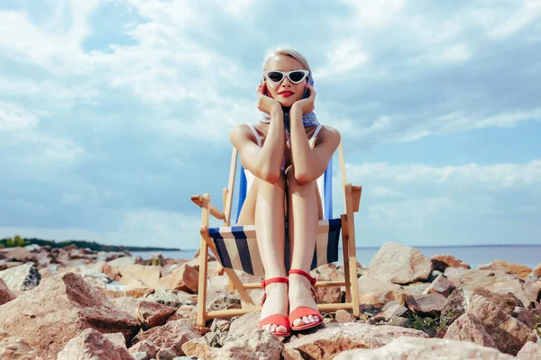 Mulher elegante atraente em maiô retro relaxante na cadeira de praia na costa rochosa — Fotografia de Stock