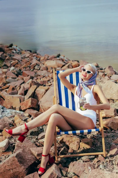 Glücklich schönes Mädchen hält Limonade und ruht sich im Strandkorb am felsigen Ufer aus — Stockfoto