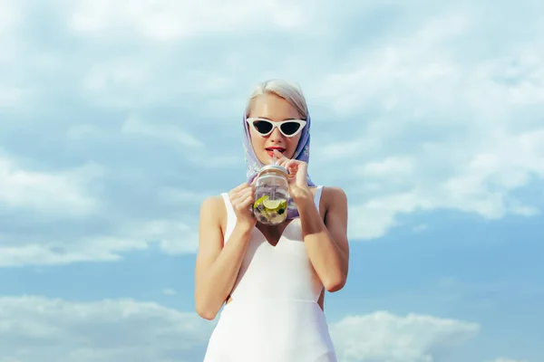Elegant girl in white retro swimsuit drinking cocktail from mason jar — Stock Photo