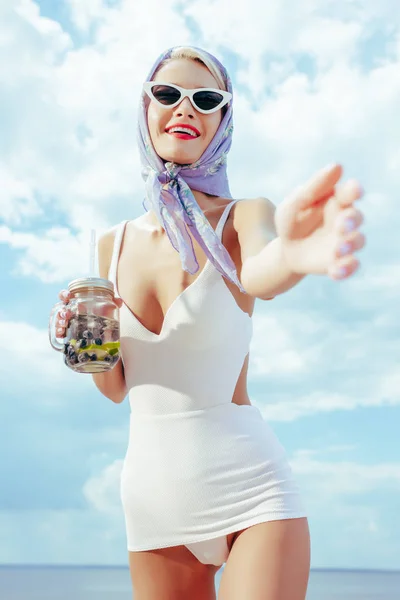 Foco seletivo da bela mulher feliz em branco vintage maiô gestos e segurando frasco de pedreiro com bebida fresca — Fotografia de Stock