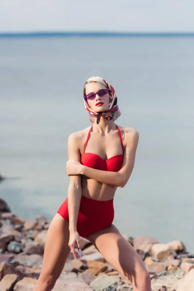 Schöne elegante Frau posiert im roten Retro-Bikini am felsigen Strand am Meer — Stockfoto