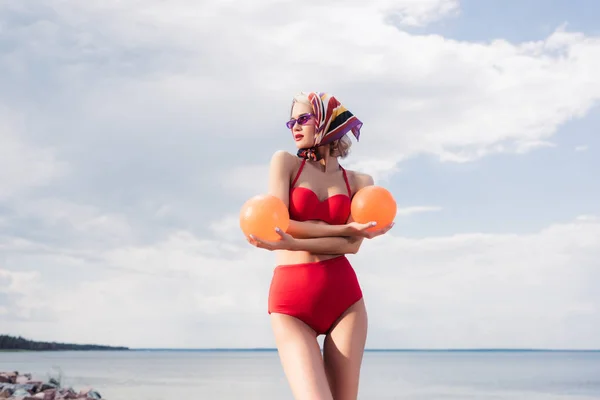 Modèle à la mode en bikini rouge et écharpe en soie posant avec des boules en mer — Photo de stock