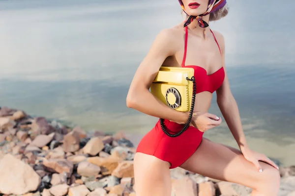 Vista recortada de la mujer en bikini rojo posando con teléfono rotatorio amarillo - foto de stock