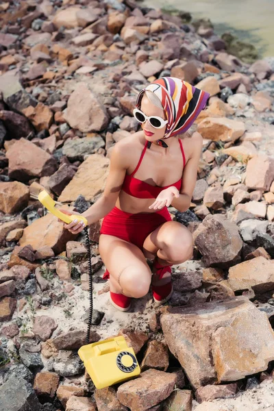 Femme en bikini rouge et écharpe en soie tenant un téléphone rotatif — Photo de stock