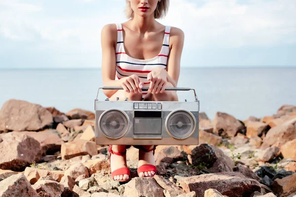 Vista ritagliata di ragazza in posa con boombox vintage sulla riva rocciosa — Foto stock